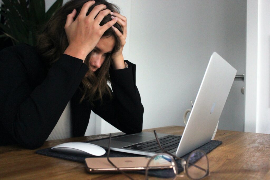 Frau sitzt gestresst und überfordert vor ihrem Laptop und stützt ihren Kopf in ihre Hände.