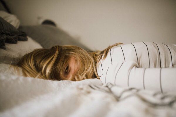 Frau liegt erschöpft im Bett (Burnout).