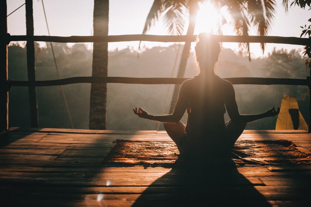 Frau im Meditationssitz unter Palmen und Sonne